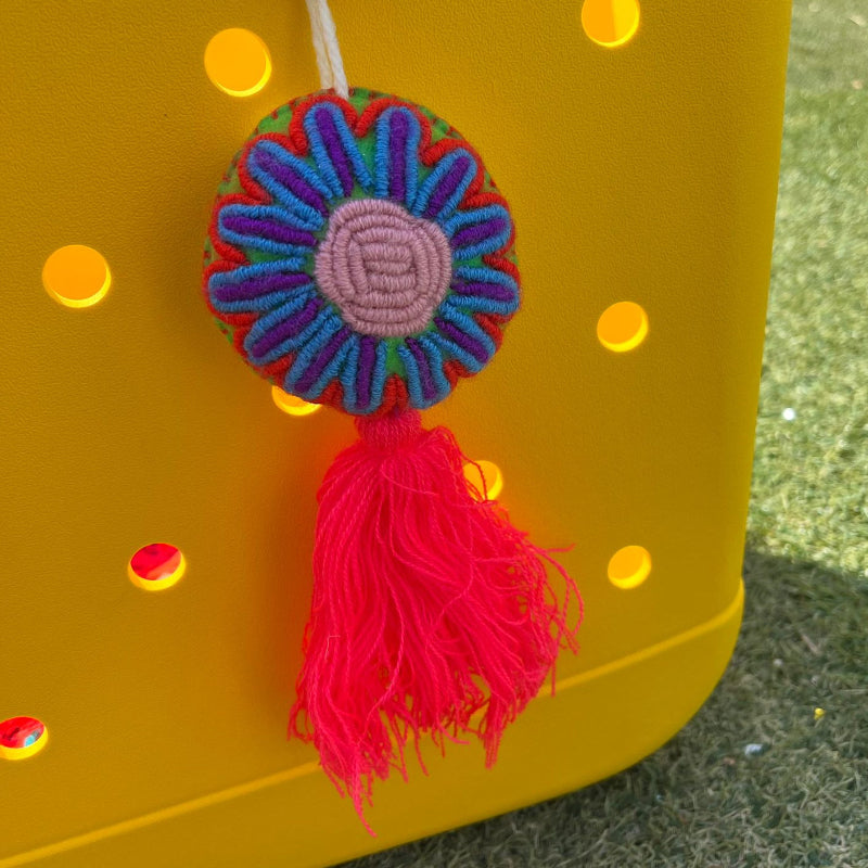 Handmade multicolor embroidered flower ornament with pastel center and red tassel on a yellow background
