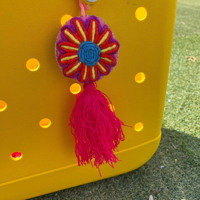 Handmade colorful embroidered flower ornament with blue center and red tassel on a yellow background