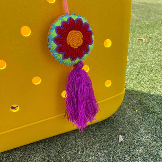 Handmade embroidered floral ornament with vibrant colors and purple tassel hanging on a yellow background