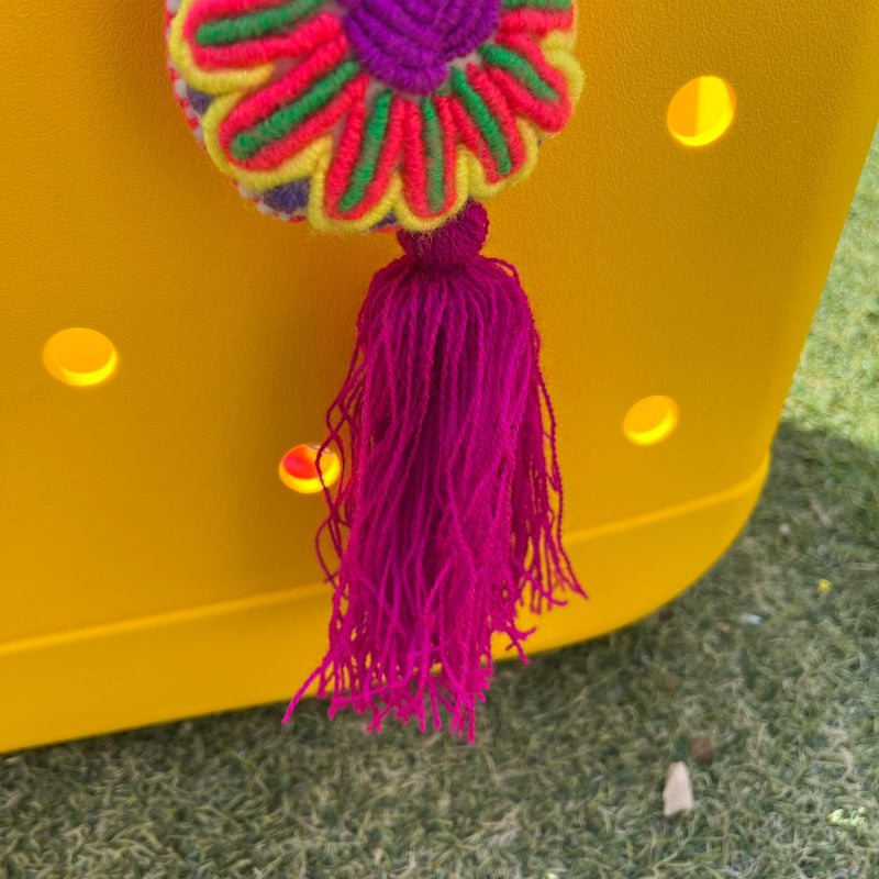 Handmade multicolor embroidered flower ornament with magenta tassel on a yellow background