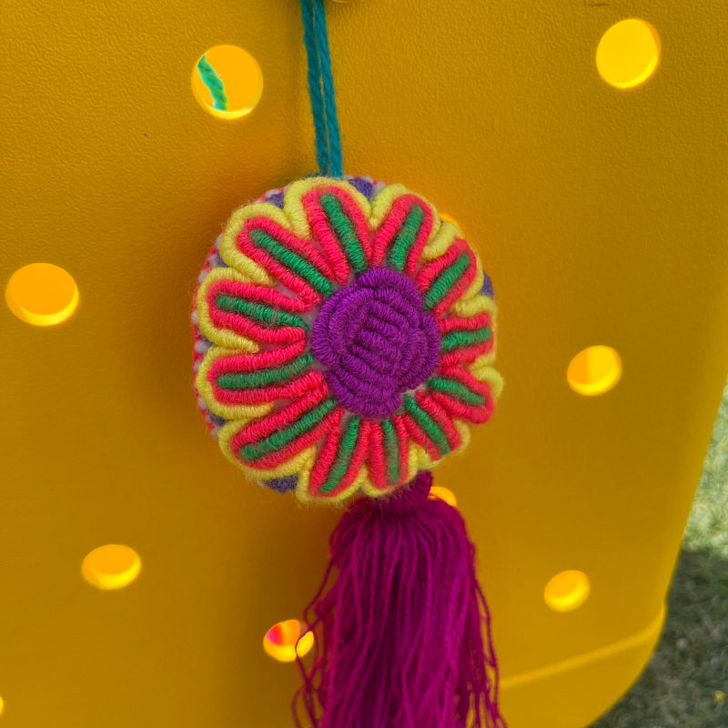 Handmade multicolor embroidered flower ornament with magenta tassel on a yellow background