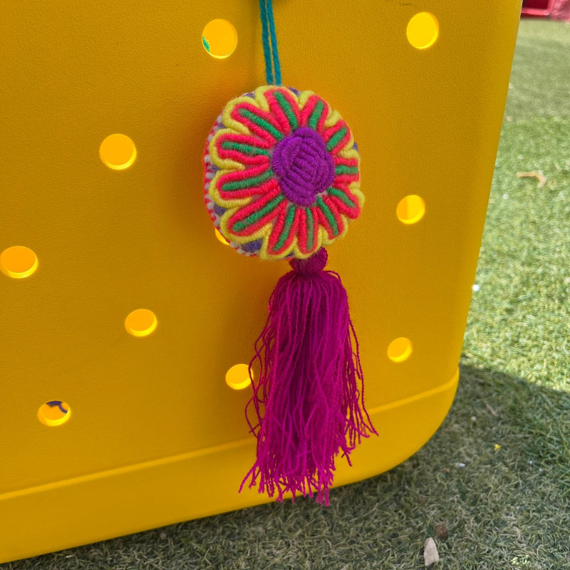 Handmade multicolor embroidered flower ornament with magenta tassel on a yellow background