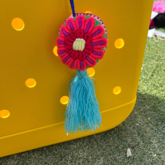 Colorful handmade embroidered flower ornament with a turquoise tassel hanging on a yellow background