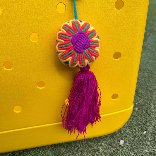 Handmade colorful embroidered floral ornament with magenta tassel hanging on a yellow background