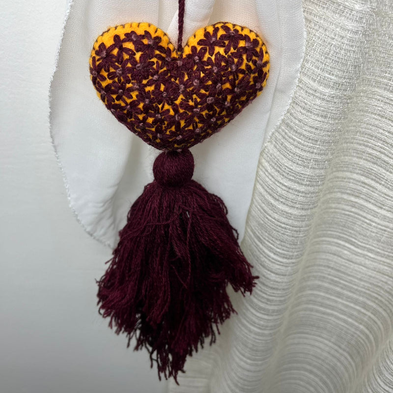 Handmade mustard embroidered heart tassel with burgundy floral stitching and matching yarn fringe on curtain