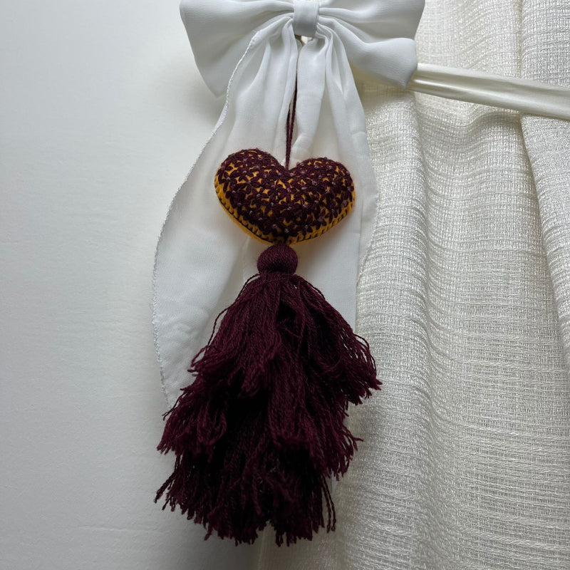 Handmade mustard embroidered heart tassel with burgundy floral stitching and matching yarn fringe on curtain