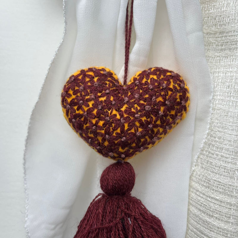 Handmade mustard embroidered heart tassel with burgundy floral stitching and matching yarn fringe on curtain