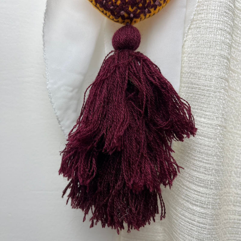 Handmade mustard embroidered heart tassel with burgundy floral stitching and matching yarn fringe on curtain