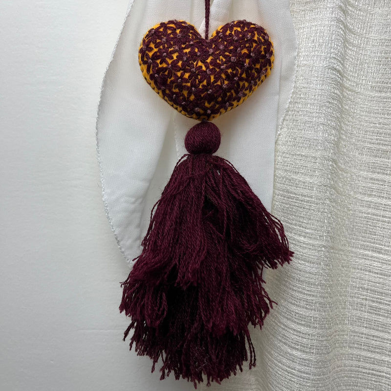Handmade mustard embroidered heart tassel with burgundy floral stitching and matching yarn fringe on curtain