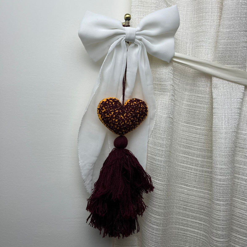 Handmade mustard embroidered heart tassel with burgundy floral stitching and matching yarn fringe on curtain