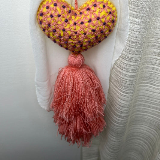 Handmade embroidered heart tassel with pink yarn fringe hanging on curtain