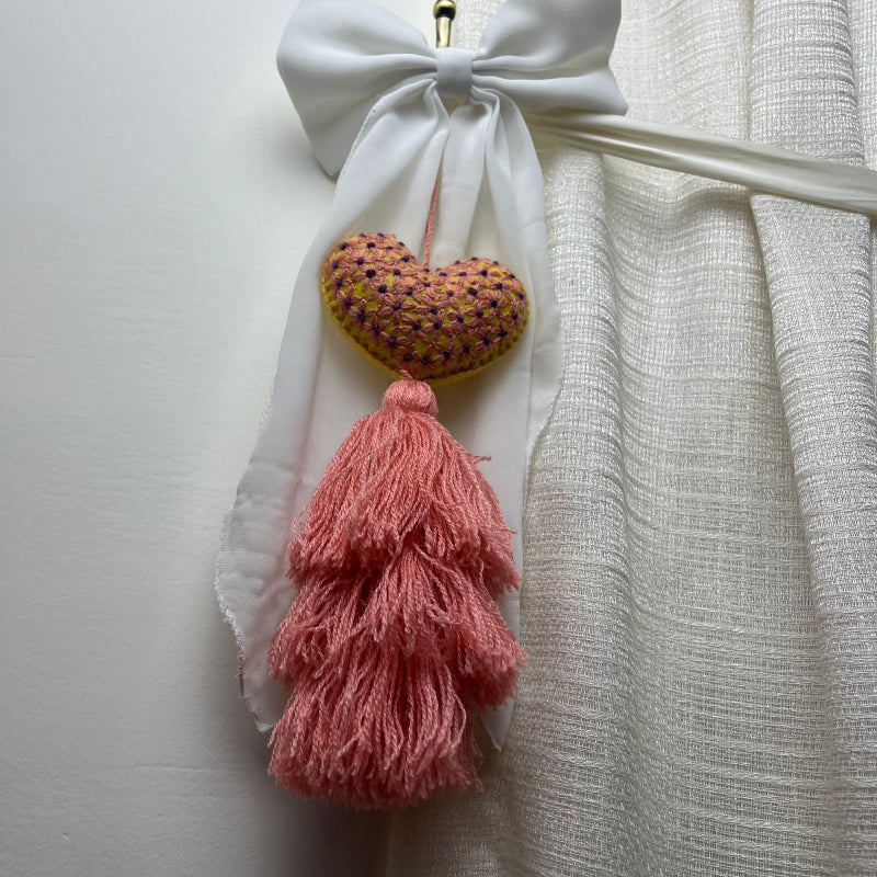 Handmade embroidered heart tassel with pink yarn fringe hanging on curtain