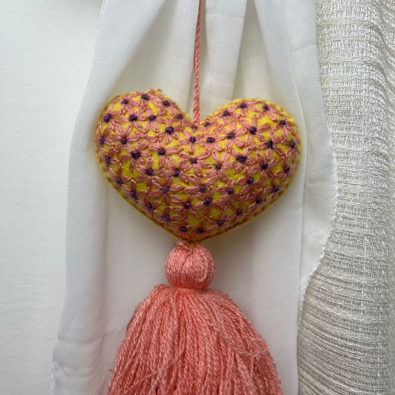 Handmade embroidered heart tassel with pink yarn fringe hanging on curtain
