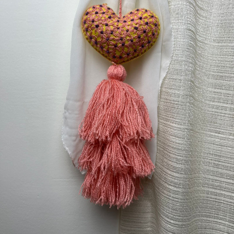Handmade embroidered heart tassel with pink yarn fringe hanging on curtain