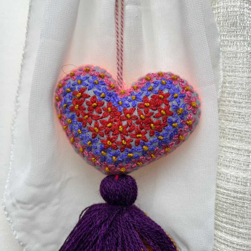Handmade multicolor embroidered heart tassel with colorful floral embroidery and layered yarn fringe on curtain