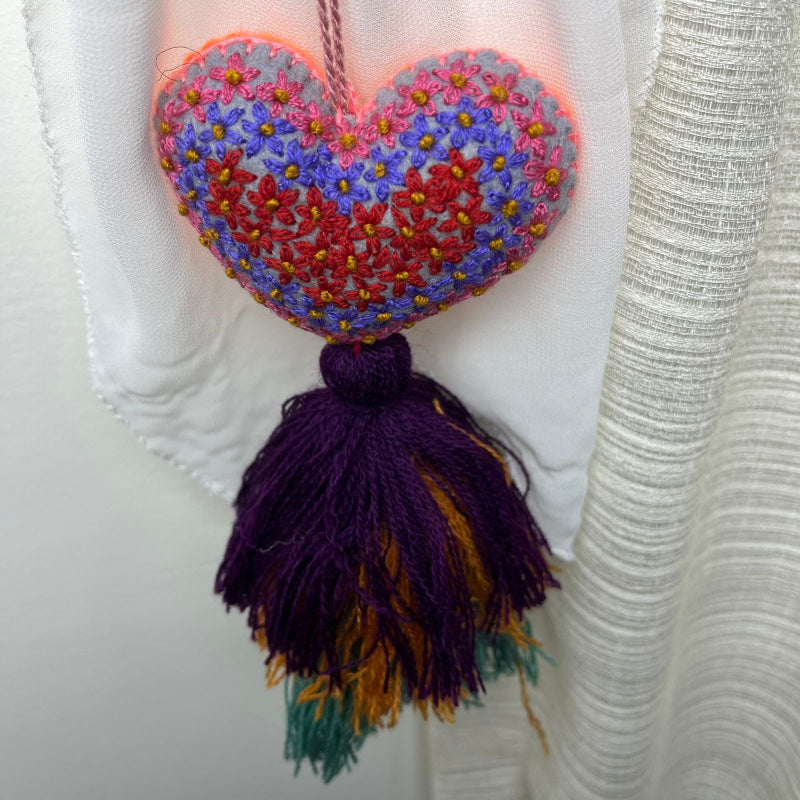 Handmade multicolor embroidered heart tassel with colorful floral embroidery and layered yarn fringe on curtain