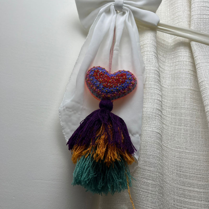 Handmade multicolor embroidered heart tassel with colorful floral embroidery and layered yarn fringe on curtain