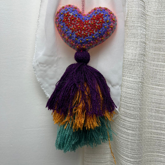 Handmade multicolor embroidered heart tassel with colorful floral embroidery and layered yarn fringe on curtain