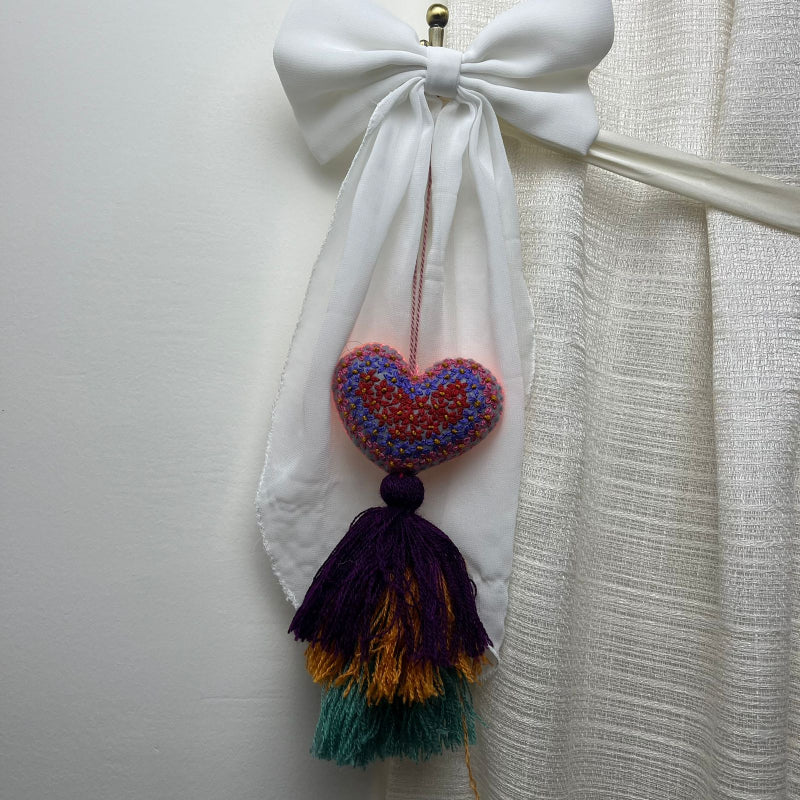 Handmade multicolor embroidered heart tassel with colorful floral embroidery and layered yarn fringe on curtain