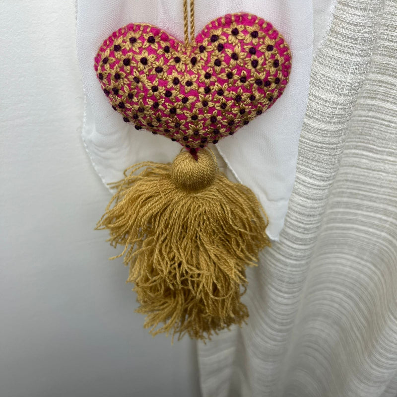 Handmade gold embroidered heart tassel with floral embroidery and gold yarn fringe on curtain