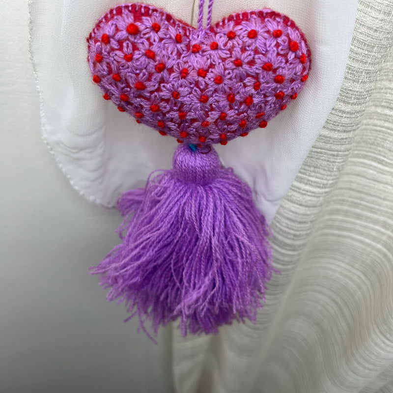 Handmade purple embroidered heart tassel with red floral embroidery and purple yarn fringe on curtain