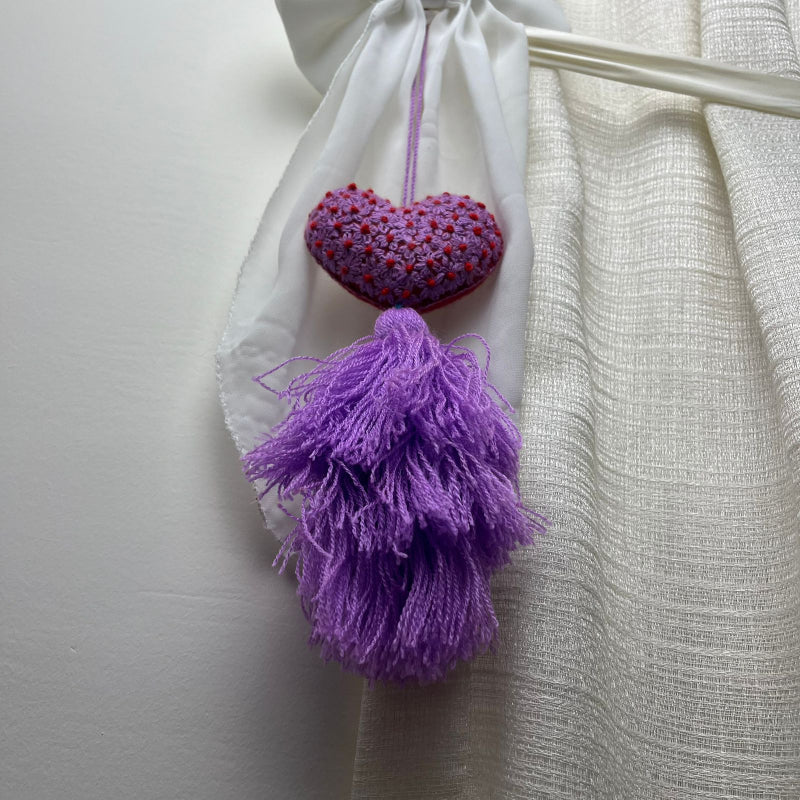 Handmade purple embroidered heart tassel with red floral embroidery and purple yarn fringe on curtain