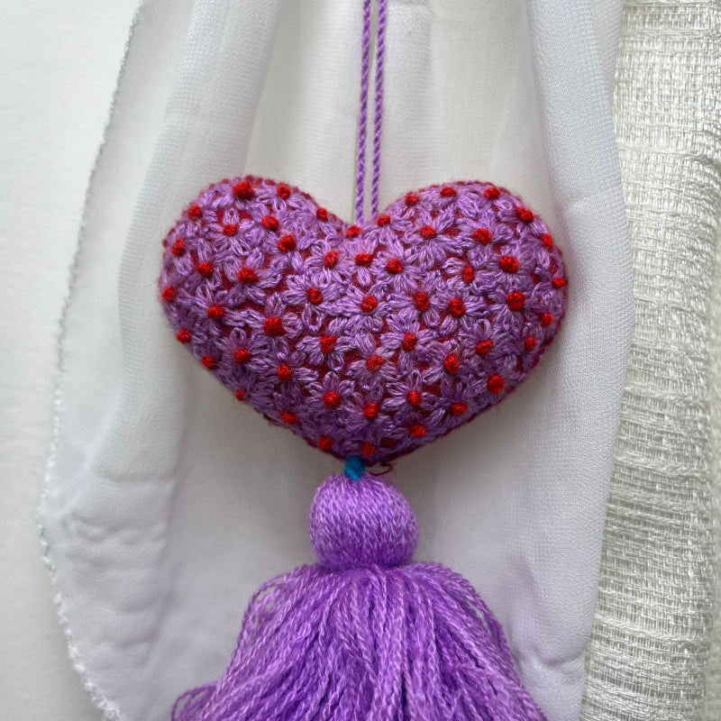 Handmade purple embroidered heart tassel with red floral embroidery and purple yarn fringe on curtain