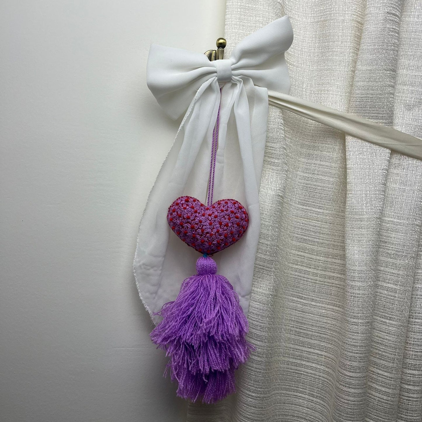 Handmade purple embroidered heart tassel with red floral embroidery and purple yarn fringe on curtain