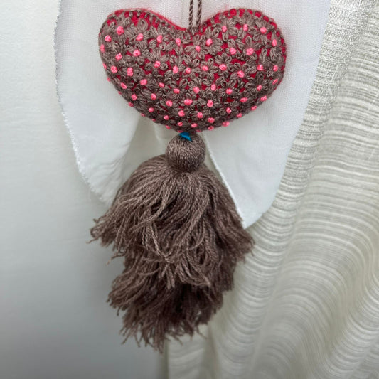 Handmade taupe embroidered heart tassel with pink floral embroidery and brown yarn fringe on curtain