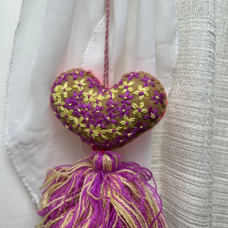 Handmade olive embroidered heart tassel with purple and yellow floral embroidery and two-tone yarn fringe on curtain