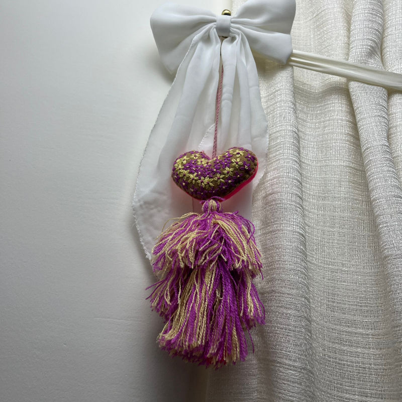 Handmade olive embroidered heart tassel with purple and yellow floral embroidery and two-tone yarn fringe on curtain