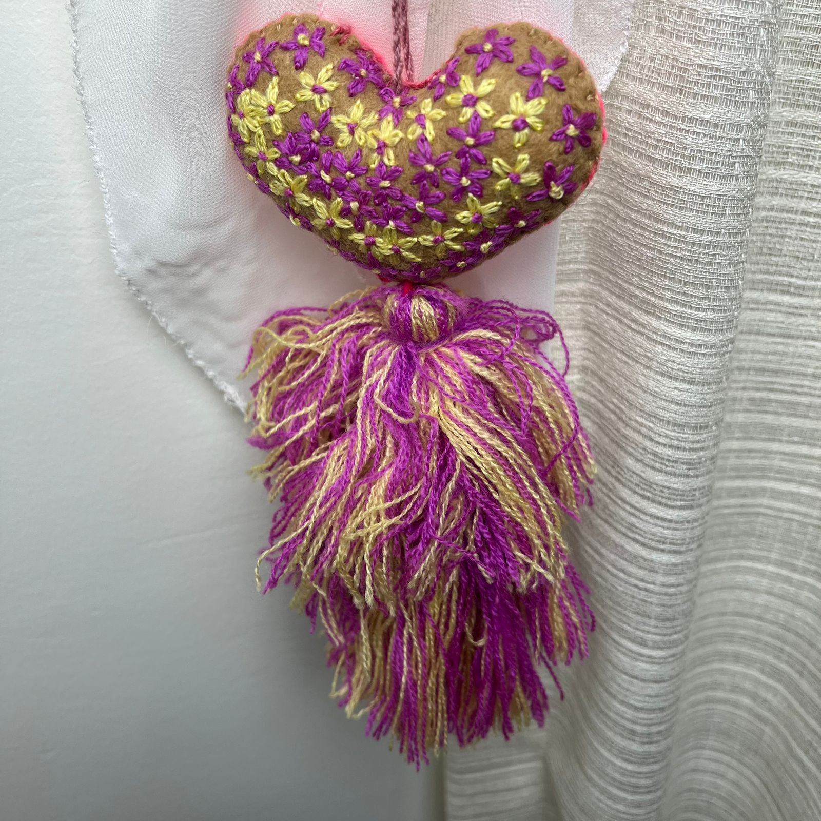 Handmade olive embroidered heart tassel with purple and yellow floral embroidery and two-tone yarn fringe on curtain