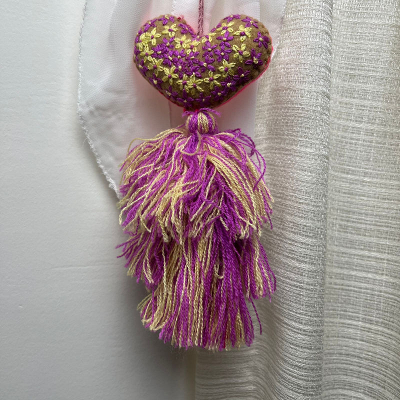Handmade olive embroidered heart tassel with purple and yellow floral embroidery and two-tone yarn fringe on curtain