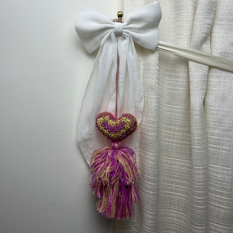 Handmade olive embroidered heart tassel with purple and yellow floral embroidery and two-tone yarn fringe on curtain