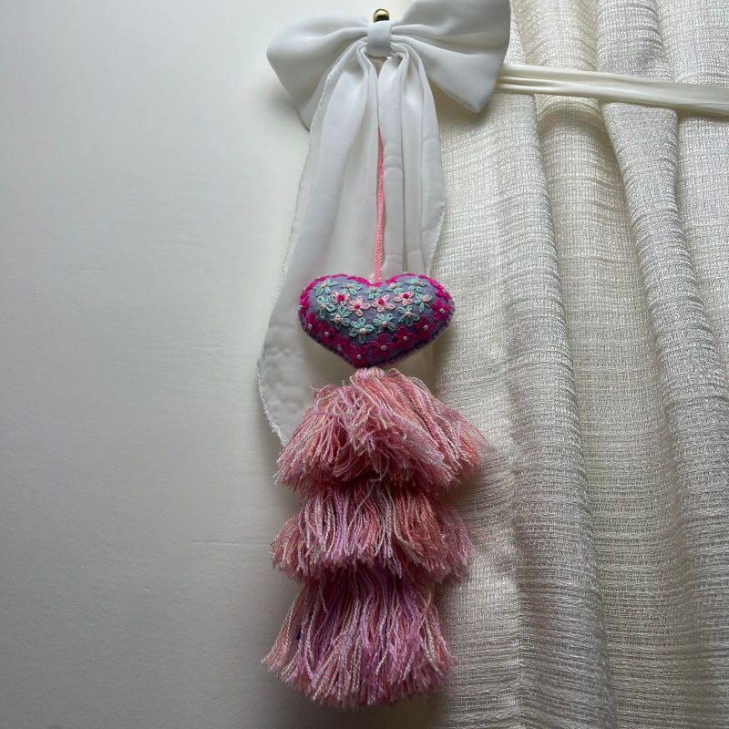 Handmade lavender embroidered heart tassel with colorful floral embroidery and pink yarn fringe on curtain