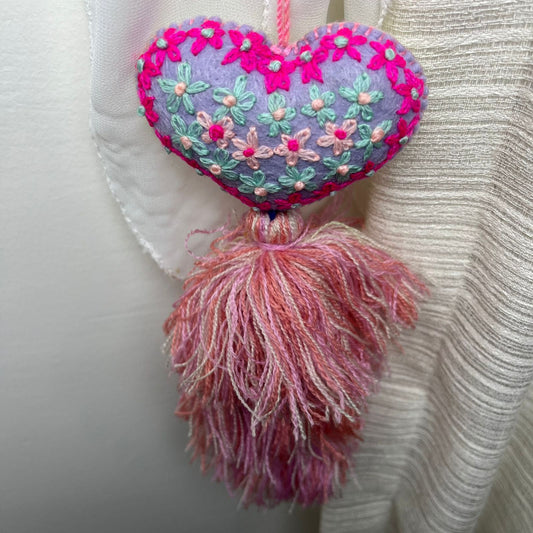 Handmade lavender embroidered heart tassel with colorful floral embroidery and pink yarn fringe on curtain
