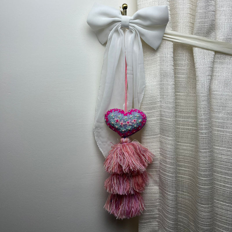 Handmade lavender embroidered heart tassel with colorful floral embroidery and pink yarn fringe on curtain