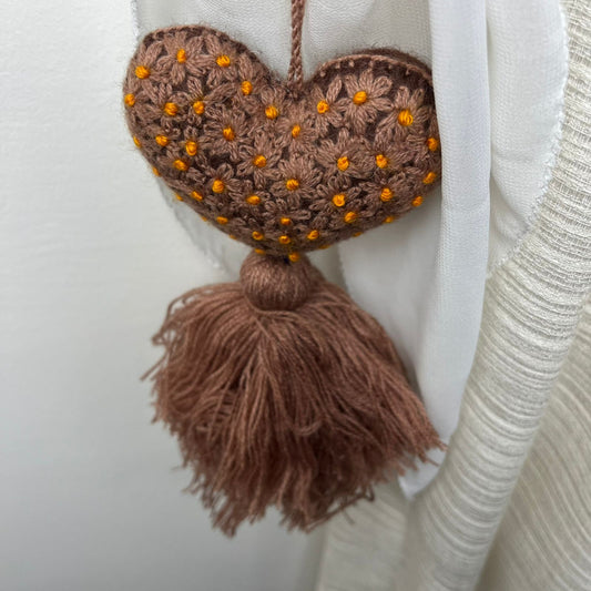Handmade brown embroidered heart tassel with golden floral details and yarn fringe on curtain