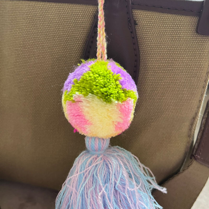 Pastel pom pom tassel bag charm with light blue and pink yarn attached to a beige handbag