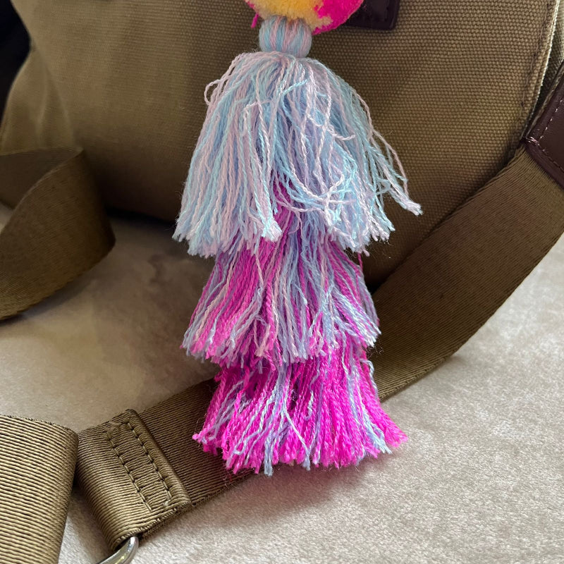 Pastel pom pom tassel bag charm with light blue and pink yarn attached to a beige handbag