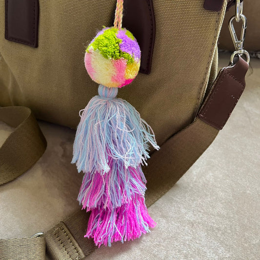 Pastel pom pom tassel bag charm with light blue and pink yarn attached to a beige handbag