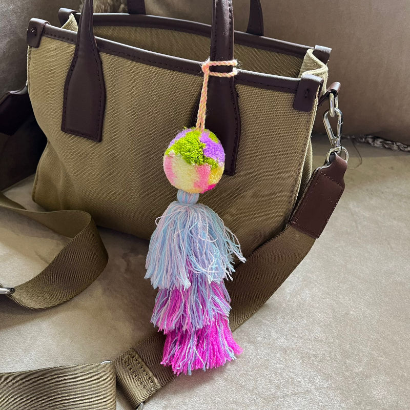 Pastel pom pom tassel bag charm with light blue and pink yarn attached to a beige handbag