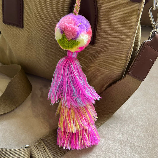 Multicolor pom pom tassel bag charm with pink layered tassels attached to a beige handbag