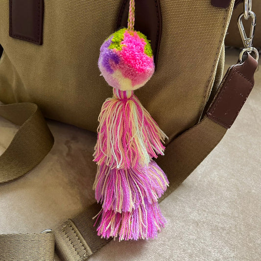 Pink pastel pom pom tassel bag charm with layered soft-toned tassels attached to a beige handbag