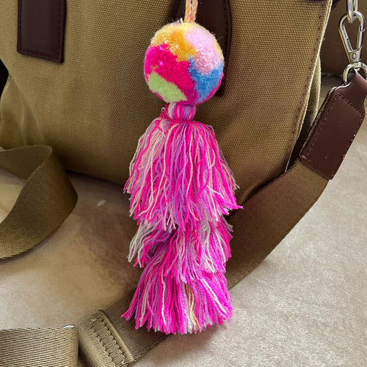 Rainbow pom pom tassel bag charm with layered pink tassels attached to a beige handbag