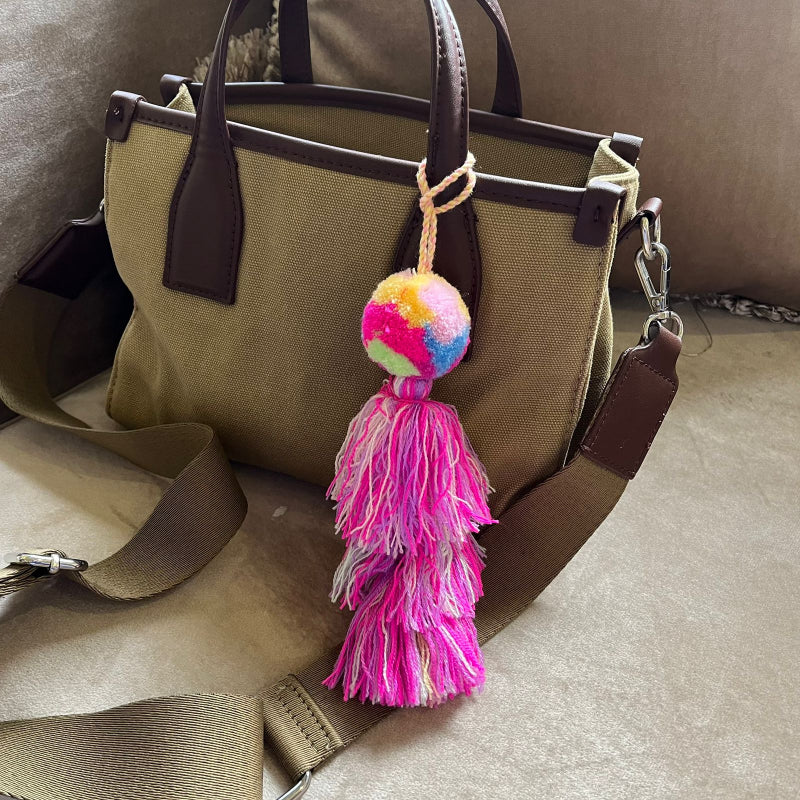 Rainbow pom pom tassel bag charm with layered pink tassels attached to a beige handbag