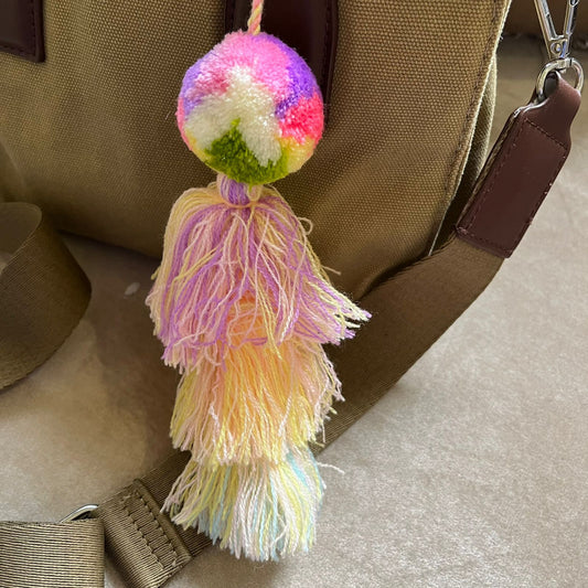 Pastel rainbow pom pom tassel bag charm with soft multicolor tassels attached to a beige handbag