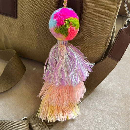 Pastel multicolor pom pom tassel bag charm with layered soft-toned tassels attached to a beige handbag