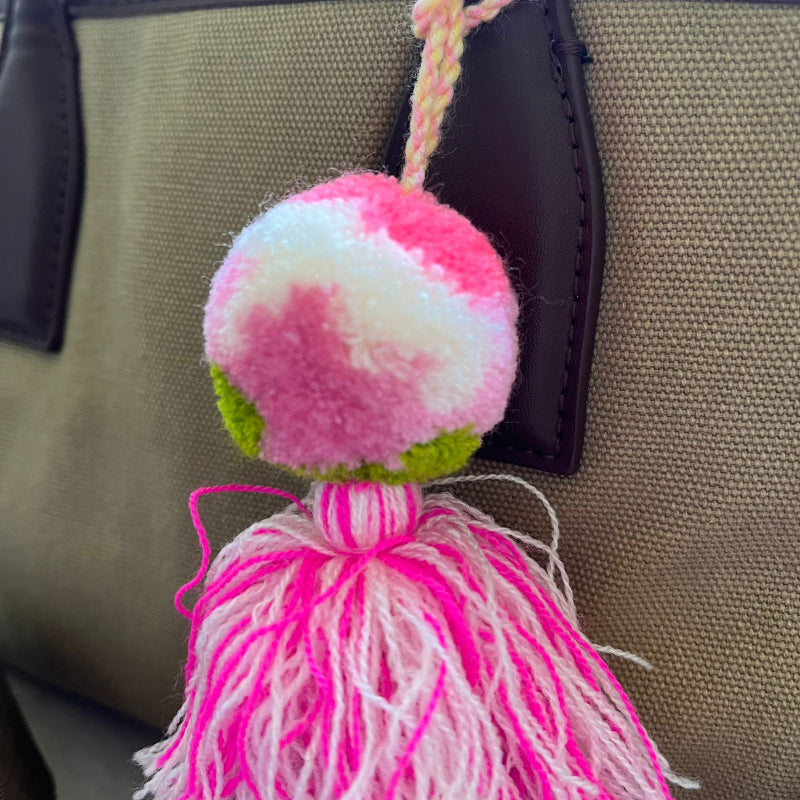Blush pink pom pom tassel bag charm with layered pink tassels attached to a beige handbag