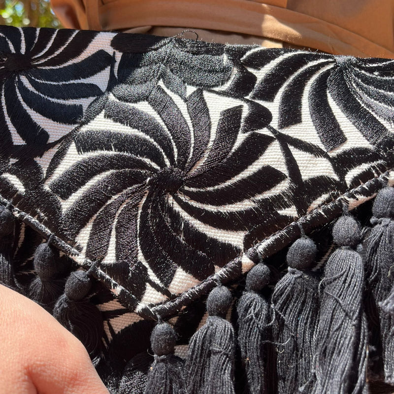 Woman holding a black and white embroidered clutch with tassels in a monochrome boho style outdoors